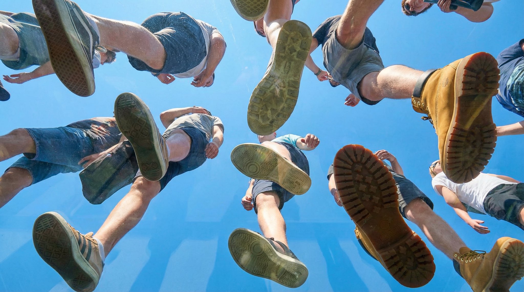 View from under a plane of completely transparent plexiglass. We are looking straight up. Many peop…